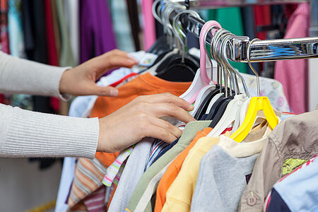weibliche Hände stöbern an hängenden Kleiderbügeln