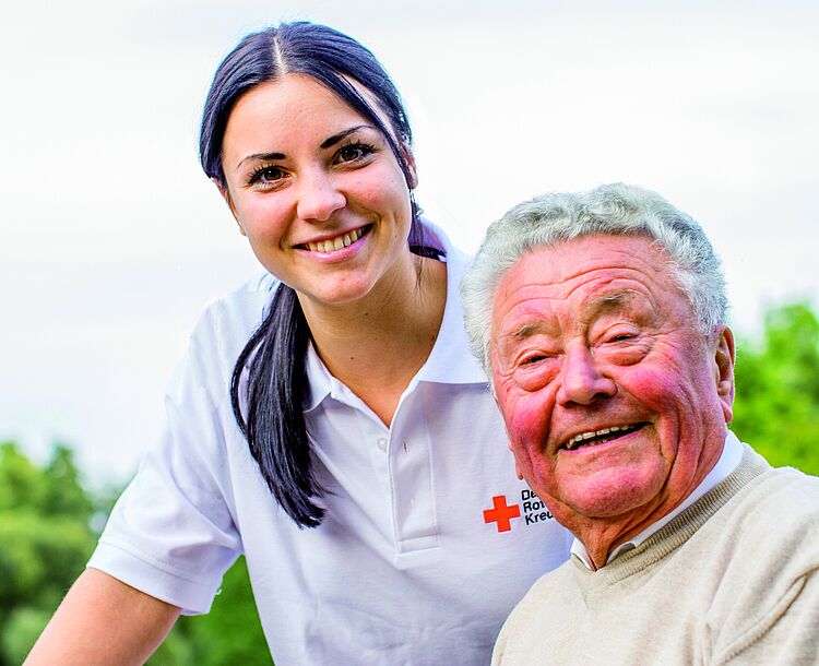 Junge DRK-Mitarbeiterin mit älterem Mann lächelnd in die Kamera schauend