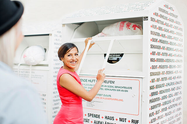 Junge Frau wirft einen Altkleidersack in einen Altkleidercontainer des Roten Kreuzes.